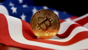 Eine goldene Bitcoin-Münze ruht aufrecht auf einer amerikanischen Flagge und symbolisiert Krypto und Kryptowährungen in den Vereinigten Staaten.
