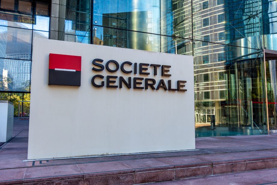 Ein Schild mit dem Logo und dem Namen der Société Générale steht vor einem gläsernen Bürogebäude und weist auf die bullische Expansion des Unternehmens in regulierte Dollar-Stablecoin-Angebote wie Société Générales USDCV hin.