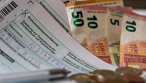 Deutsche Einkommensteuerformulare, Euro-Banknoten, ein Stift, Euro-Münzen und Krypto-Dokumente liegen auf einem Schreibtisch.