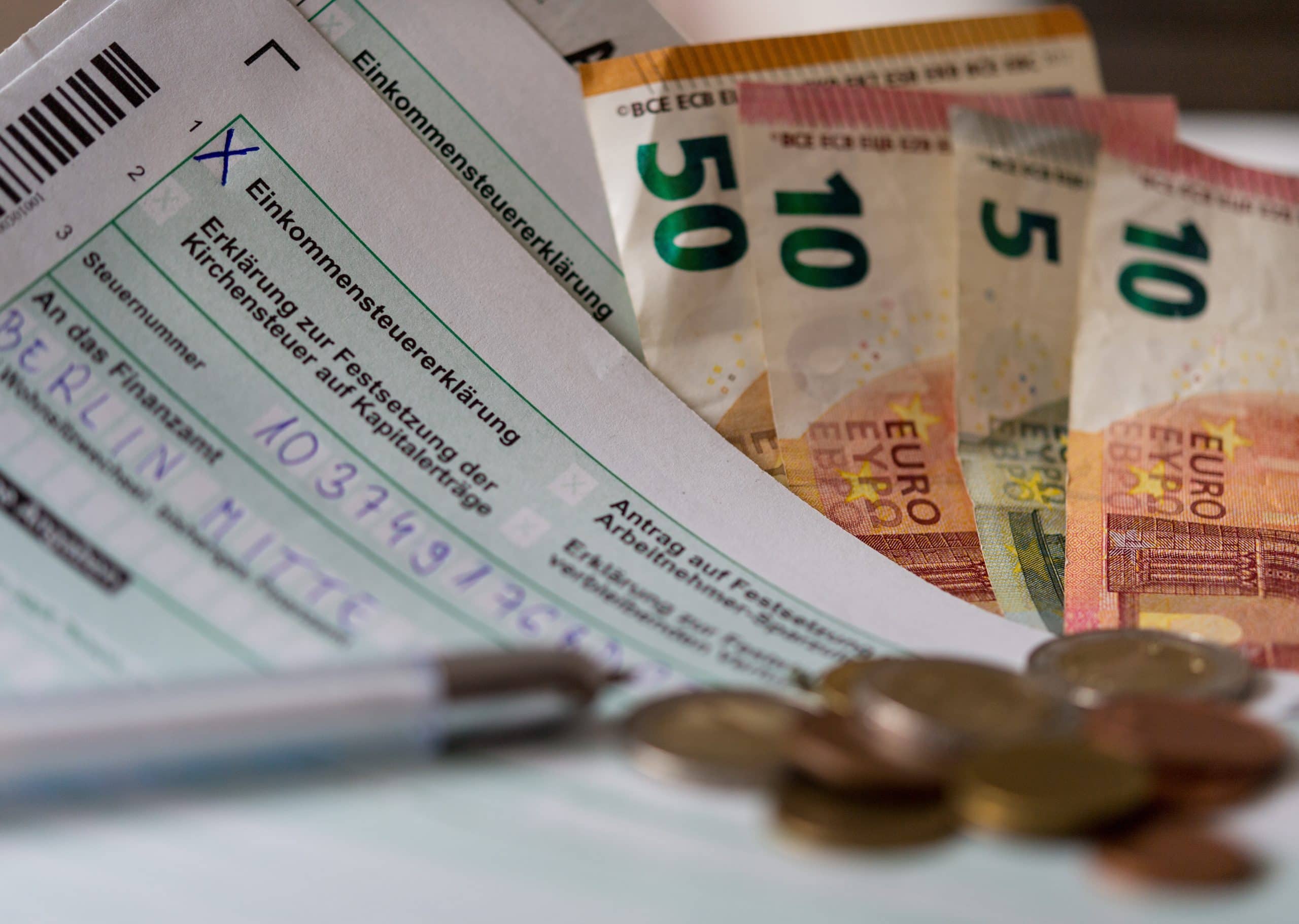 Deutsche Einkommensteuerformulare, Euro-Banknoten, ein Stift, Euro-Münzen und Krypto-Dokumente liegen auf einem Schreibtisch.