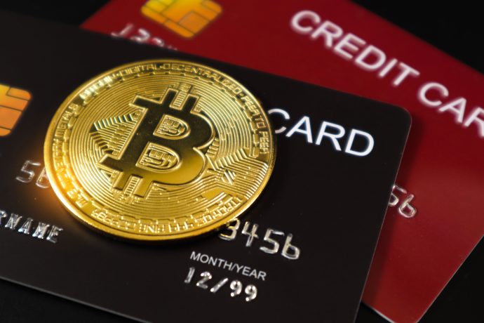 Ein goldener Bitcoin-Token ruht auf zwei gestapelten Kreditkarten und verdeutlicht die Überschneidung von Bitcoin und traditionellen Finanzsystemen.