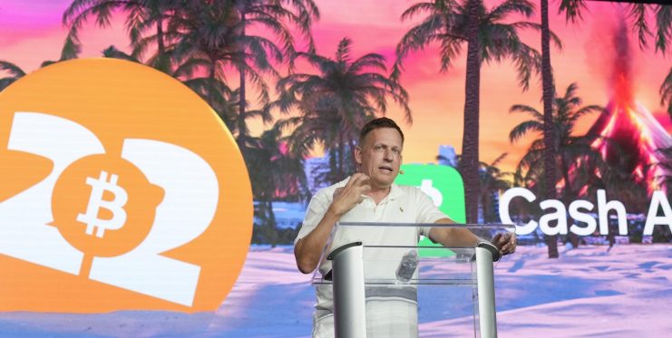 Ein Redner steht an einem Podium vor einem Bildschirm, auf dem das Logo der Bitcoin 2022-Konferenz, das Cash App-Logo und ein dynamisches Krypto-Branding vor einem tropischen Hintergrund mit Bühnenbeleuchtung zu sehen sind.