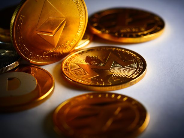 Mehrere goldfarbene Kryptowährungsmünzen, darunter Ethereum, Monero und andere beliebte Altcoins, sind auf einer weißen Fläche angeordnet.