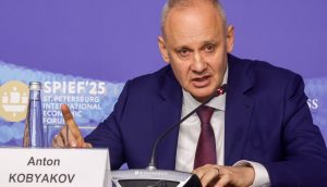 Ein Mann im blauen Anzug und mit roter Krawatte (Anton Kobyakov) spricht während einer Pressekonferenz zu einem Mikrofon. Auf einem Namensschild steht Anton Kobyakov. Im Hintergrund ist ein Schild des Internationalen Wirtschaftsforums in St. Petersburg zu sehen, einer Veranstaltung, an der auch Putin teilnimmt.