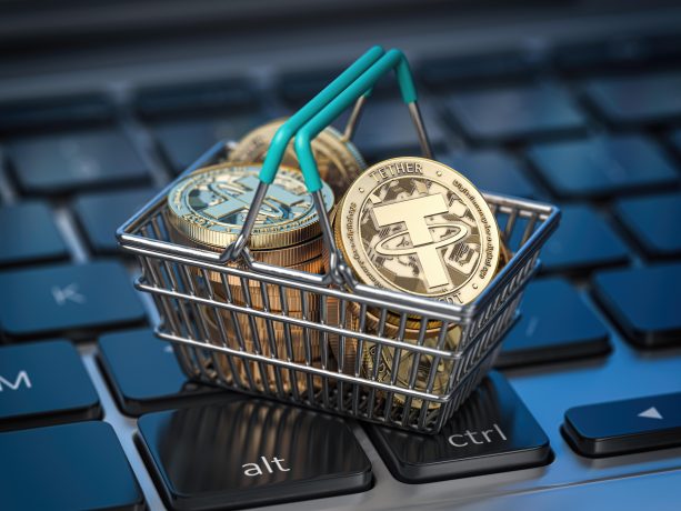 Ein kleiner, mit goldfarbenen Tether-Stablecoins gefüllter Einkaufskorb steht auf einer Computertastatur. Er verdeutlicht die Abhängigkeit der digitalen Wirtschaft von Stablecoins und wirft Fragen zu Schattenbanken im Kryptobereich auf.