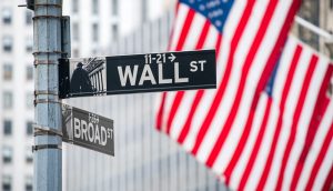 Schild der Wall Street mit USA-Flagge im Hintergrund
