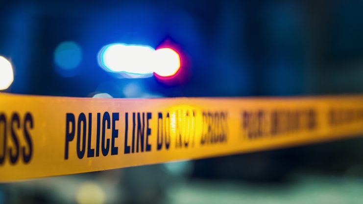 Nahaufnahme der gelben "beschlagnahmt" Polizei Linie nicht überqueren Band mit verschwommenen blauen und roten UK-Polizei Lichter im Hintergrund in der Nacht.