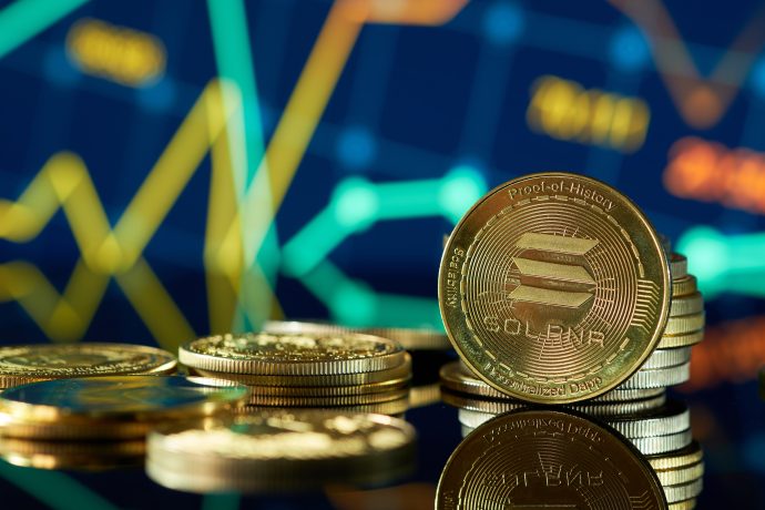 Stapel von Solana-Kryptowährungsmünzen sind vor einem digitalen Bildschirm ausgestellt, der bunte, schwankende Solana-Finanzdiagramme zeigt.