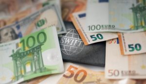 Mehrere Euro- und Dollarscheine umgeben ein metallisches SWIFT-Logo, das internationale Finanztransaktionen, Bankensysteme (Banken) und den wachsenden Einfluss von Stablecoins im globalen Finanzwesen symbolisiert.