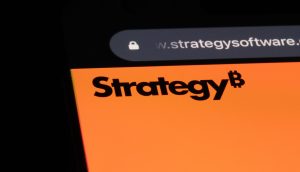Auf dem Bildschirm eines Smartphones wird eine Website angezeigt, auf der in fetten schwarzen Buchstaben auf orangefarbenem Hintergrund das Wort "Strategy" (Strategie) zu lesen ist, mit einem Bitcoin-Symbol als Buchstabe B - gekennzeichnet als automatisch gespeicherter Entwurf.
