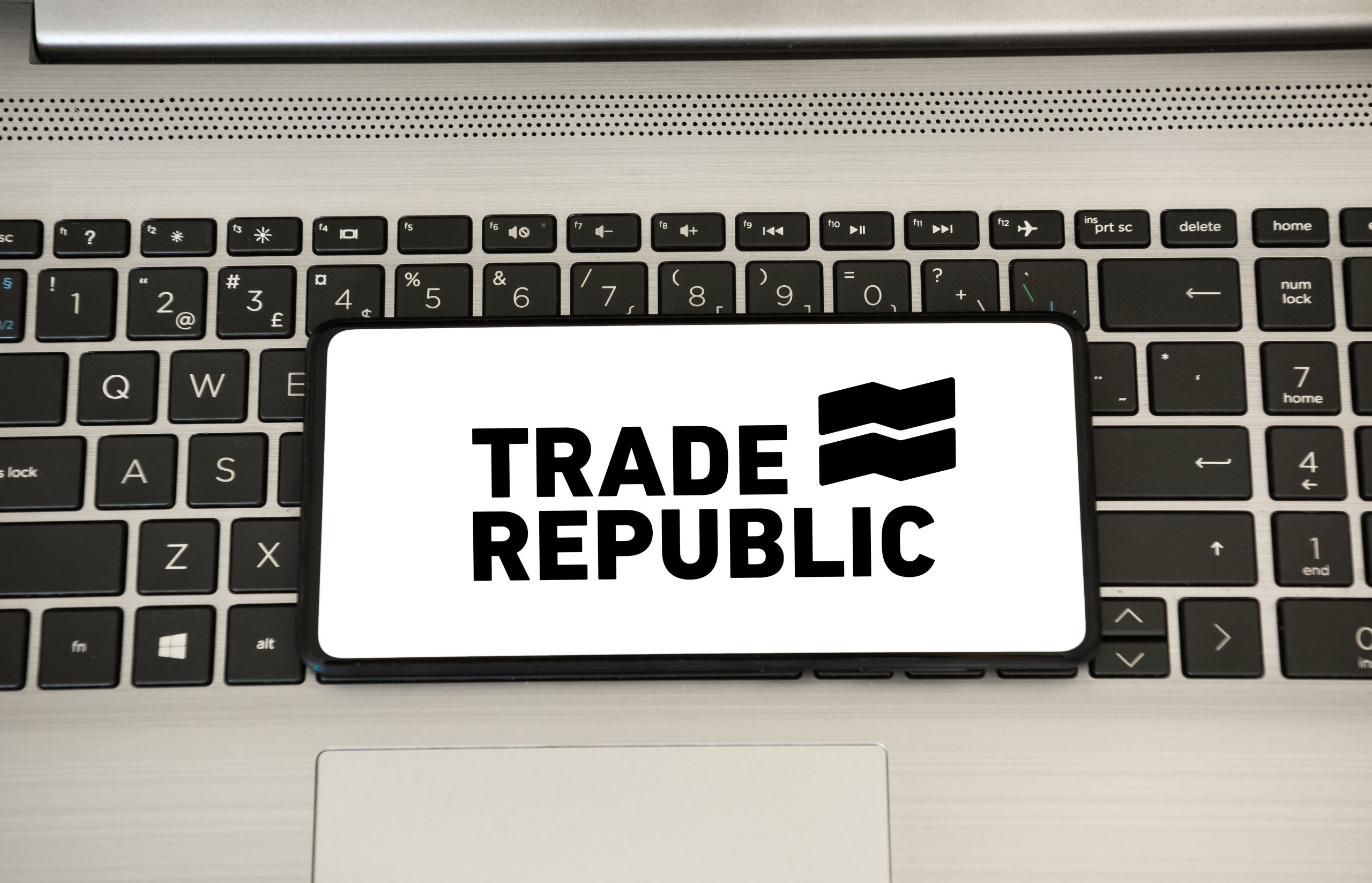 Ein Smartphone mit dem Logo Trade Republic liegt auf der Tastatur eines Laptops: ein Symbolbild für den Trade Republic Sparplan.