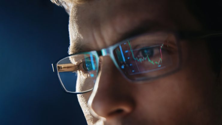 Nahaufnahme eines Traders mit Brille, in deren Gläsern Kurscharts reflektieren. Symbolbild für Spannung und Konzentration beim Krypto-Trading.