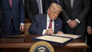 Donald Trump sitzt an einem Schreibtisch mit dem Siegel des Präsidenten und unterschreibt ein Dokument. Umgeben von anderen Männern in Anzügen, schließt er eine Vereinbarung über Trump Media im Wert von 105 Millionen US-Dollar ab.