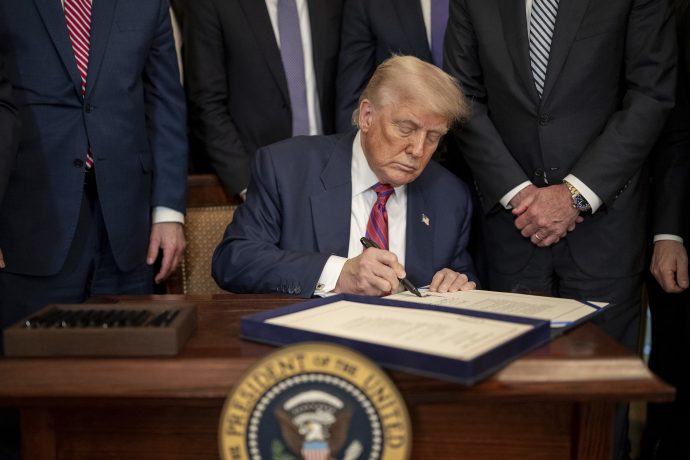 Donald Trump sitzt an einem Schreibtisch mit dem Siegel des Präsidenten und unterschreibt ein Dokument. Umgeben von anderen Männern in Anzügen, schließt er eine Vereinbarung über Trump Media im Wert von 105 Millionen US-Dollar ab.
