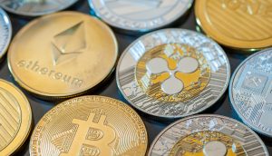 Nahaufnahme verschiedener physischer Krypto-Münzen, darunter Bitcoin, Ethereum, Litecoin und Ripple, die in Reihen auf einer reflektierenden Oberfläche angeordnet sind.