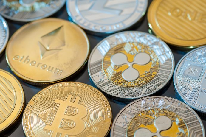 Nahaufnahme verschiedener physischer Krypto-Münzen, darunter Bitcoin, Ethereum, Litecoin und Ripple, die in Reihen auf einer reflektierenden Oberfläche angeordnet sind.
