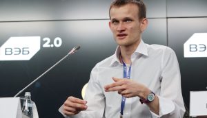 Bringt Low-Risk-DeFi die nächste Adoptionswelle für Ethereum? Vitalik Buterin in einem weißen Hemd spricht auf einer Ethereum-Konferenz und gestikuliert mit den Händen. Er sitzt an einem Tisch mit einem Mikrofon und einem Namensschild vor einem Hintergrund mit der Aufschrift 2.0.