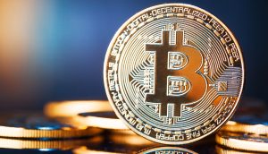 Nahaufnahme eines physischen Bitcoins mit dem Bitcoin-Logo auf einer spiegelnden Oberfläche, mit anderen Münzen im Hintergrund, die leicht verschwommen sind.