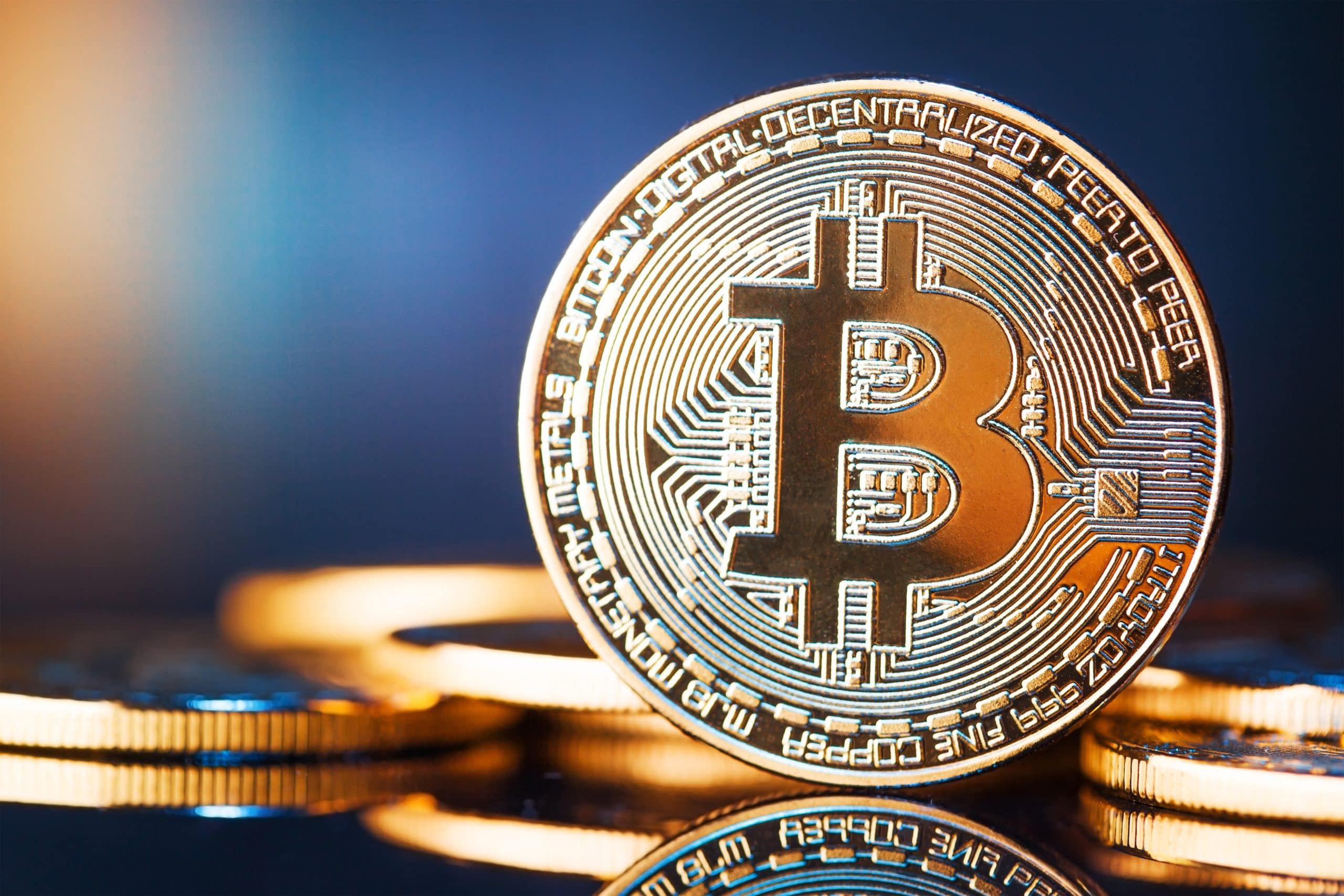 Nahaufnahme einer aufrecht stehenden physischen Bitcoin-Münze mit kreisförmigem Design, andere Münzen im Hintergrund, auf einer spiegelnden Oberfläche, die die besonderen Merkmale von Bitcoin hervorhebt.