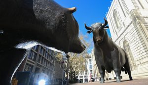 Eine Bären- und eine Bullenstatue aus Bronze stehen sich auf einer Straße in der Stadt gegenüber und symbolisieren gegensätzliche Trends auf dem Aktienmarkt und den Aufstieg der Blockchain-Technologie. Gebäude und ein klarer Himmel sorgen für eine moderne Kulisse.