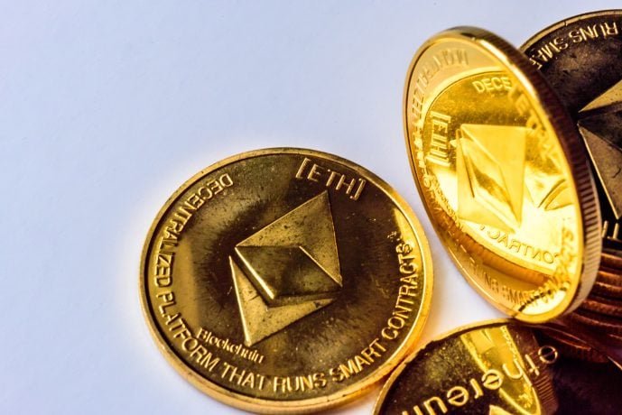 Eine Nahaufnahme mehrerer goldglänzender Ethereum-Münzen, auf deren Oberfläche das Ethereum-Logo und DECENTRALIZED PLATFORM THAT RUNS SMART CONTRACTS eingraviert sind.