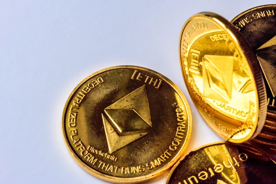Eine Nahaufnahme mehrerer goldglänzender Ethereum-Münzen, auf deren Oberfläche das Ethereum-Logo und DECENTRALIZED PLATFORM THAT RUNS SMART CONTRACTS eingraviert sind.