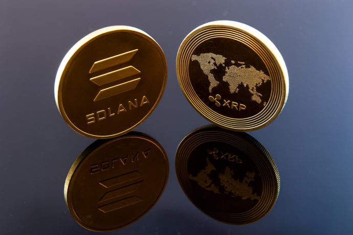 Zwei Münzen mit den Logos der Kryptowährungen Solana und XRP, die auf jeder ETF-Beobachtungsliste zu finden sind, stehen aufrecht auf einer reflektierenden schwarzen Oberfläche.