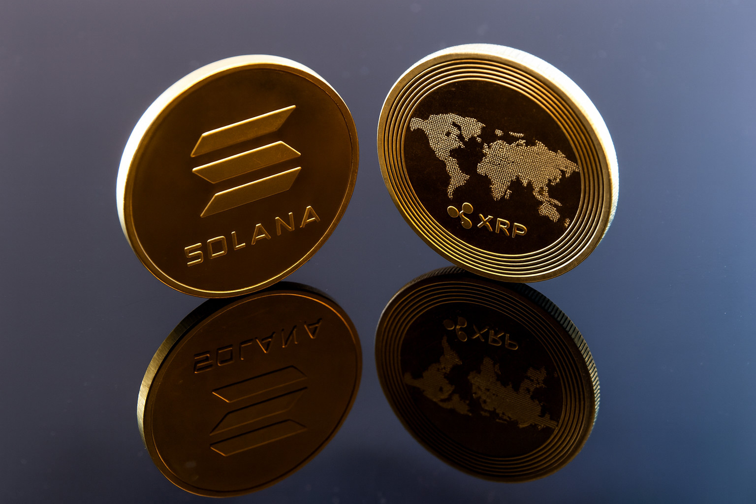 Zwei Münzen mit den Logos der Kryptowährungen Solana und XRP, die auf jeder ETF-Beobachtungsliste zu finden sind, stehen aufrecht auf einer reflektierenden schwarzen Oberfläche.