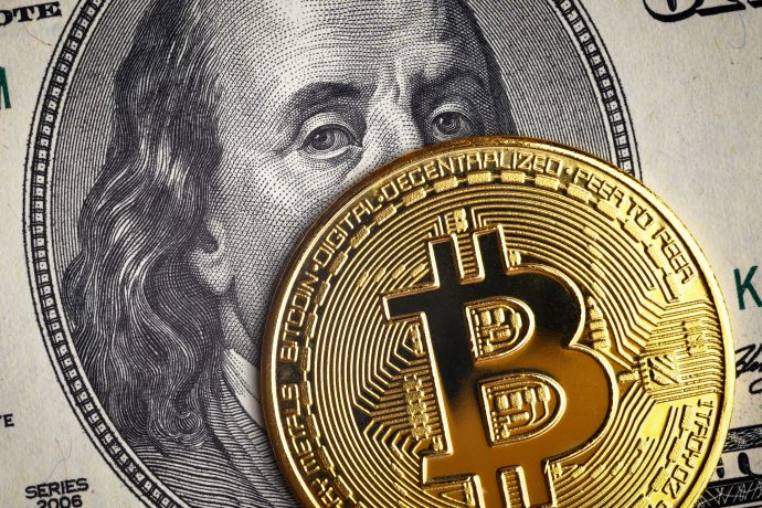 Eine goldene Bitcoin-Münze bedeckt teilweise einen US-Hundert-Dollar-Schein mit dem Gesicht Benjamin Franklins und symbolisiert damit die Überschneidung von Krypto und traditionellen Finanzen.