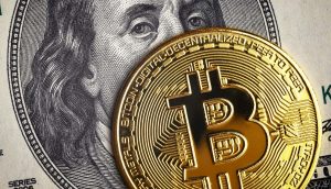 Eine goldene Bitcoin-Münze bedeckt teilweise einen US-Hundert-Dollar-Schein mit dem Gesicht Benjamin Franklins und symbolisiert damit die Überschneidung von Krypto und traditionellen Finanzen.