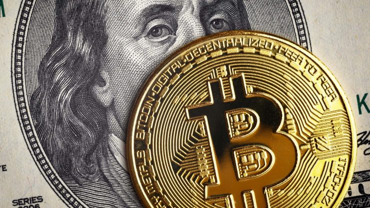 Eine goldene Bitcoin-Münze bedeckt teilweise einen US-Hundert-Dollar-Schein mit dem Gesicht Benjamin Franklins und symbolisiert damit die Überschneidung von Krypto und traditionellen Finanzen.