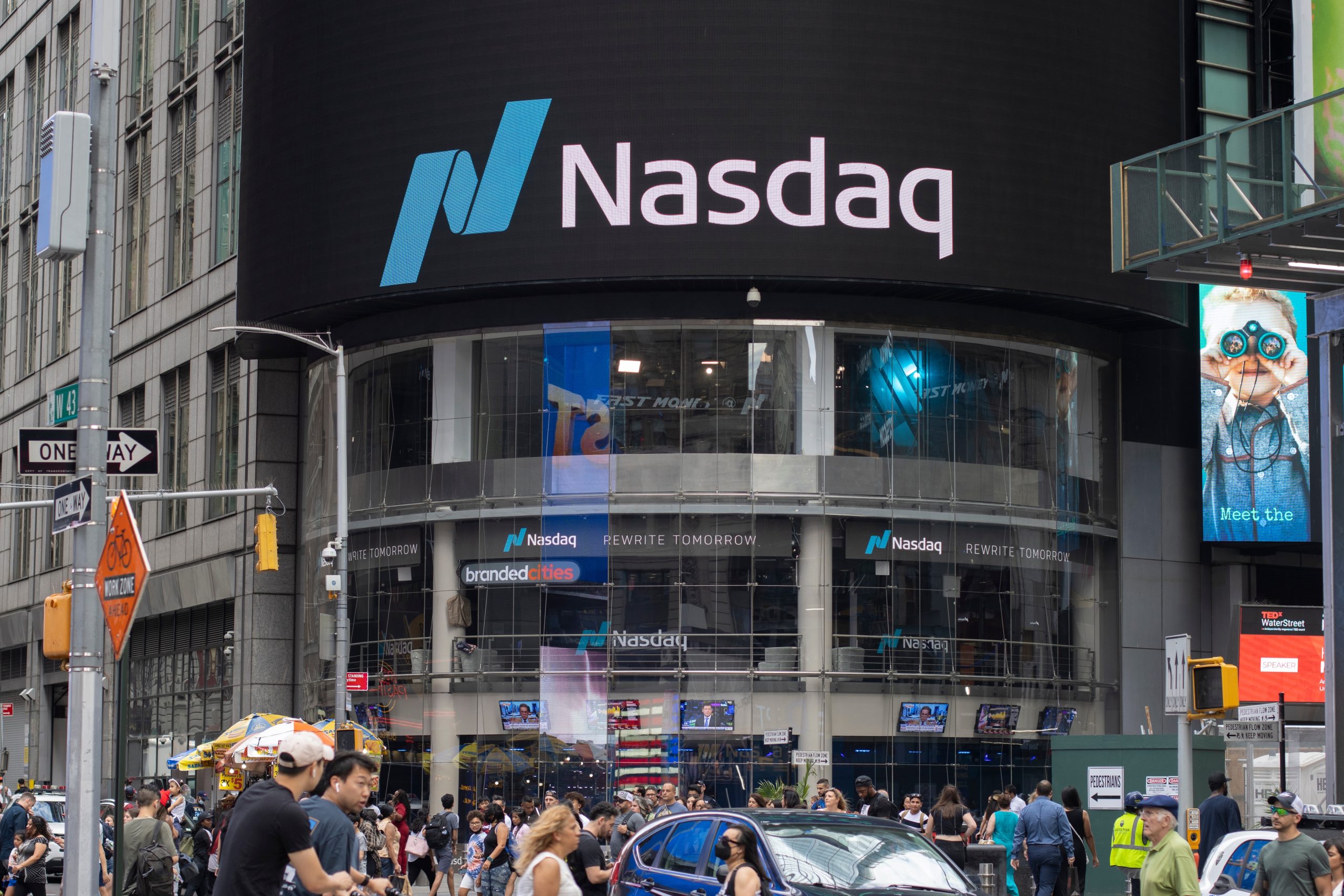 Neben Securitize sind in 2025 schon viele Krypto-Unternehmen an die Börse gegangen. Straßenansicht des Nasdaq MarketSite-Gebäudes am Times Square, New York City, mit den großen Logos von Nasdaq und Securitize auf einem LED-Bildschirm über dem regen Fußgängerverkehr.
