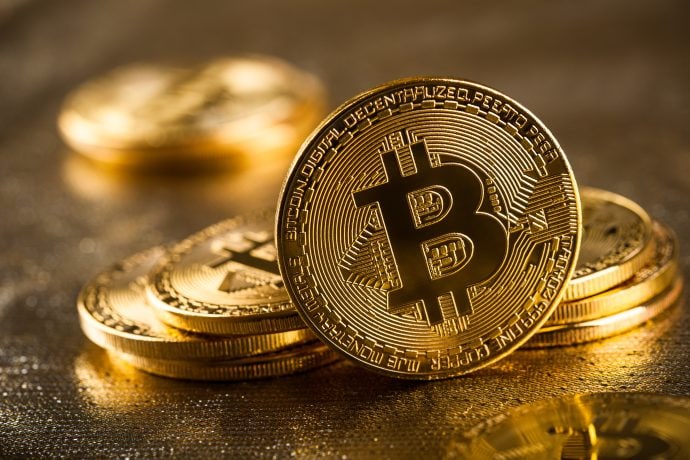 Gestapelte und aufrecht stehende goldfarbene Münzen zeigen das Bitcoin-Symbol mit detaillierten Gravuren vor einem verschwommenen goldenen Hintergrund - ein inspirierendes Bild für jeden, der eine Bitcoin-Investition in Erwägung zieht oder 2024 in Bitcoin investieren möchte.