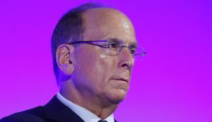 Larry Fink mittleren Alters im Anzug und mit Brille blickt vor einem kräftigen lila Hintergrund nach vorne und denkt über die steigende Nachfrage nach innovativen Anlagemöglichkeiten wie Krypto-ETFs nach.