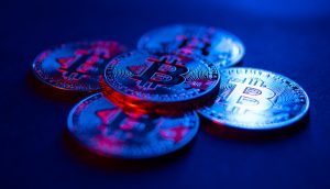 Fünf metallische Bitcoin-Münzen sind auf einer dunklen Fläche angeordnet, die mit blauem und rotem Licht beleuchtet wird und an die High-Tech-Welt der Kryptoanalyse und Unternehmen wie Chainalysis erinnert.