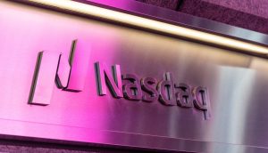 Ein Metallschild zeigt das Nasdaq-Logo und den Namen, beleuchtet von rosa und violettem Licht, das an die geschäftige Atmosphäre einer Krypto-Börse erinnert.