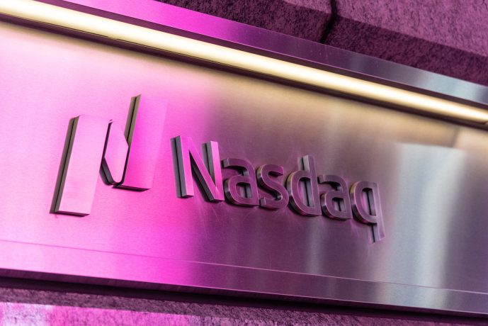 Ein Metallschild zeigt das Nasdaq-Logo und den Namen, beleuchtet von rosa und violettem Licht, das an die geschäftige Atmosphäre einer Krypto-Börse erinnert.