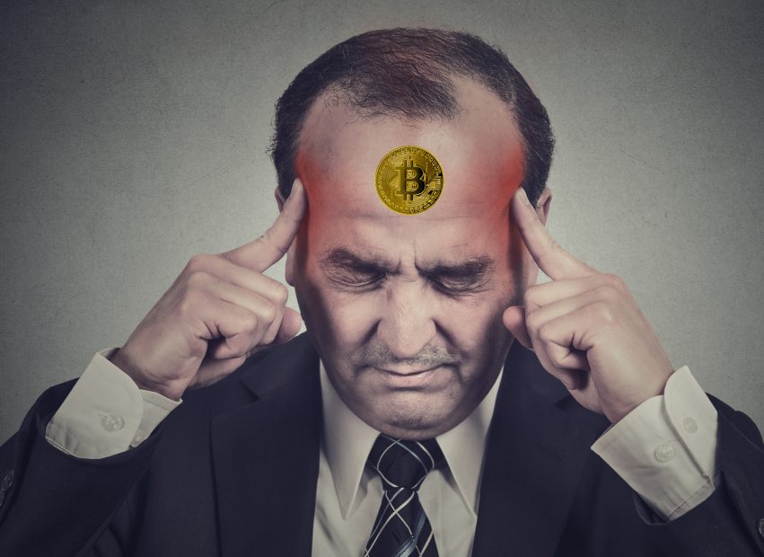 Ein Mann im Anzug berührt seine Schläfen und runzelt die Stirn. Auf seiner Stirn ist das Bitcoin-Symbol digital dargestellt.