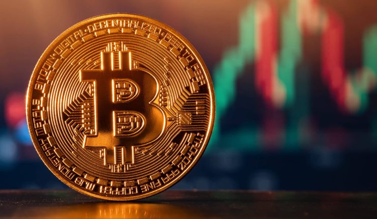 Eine goldene Bitcoin-Münze wird vor einem unscharfen Hintergrund mit bunten Finanzcharts angezeigt.