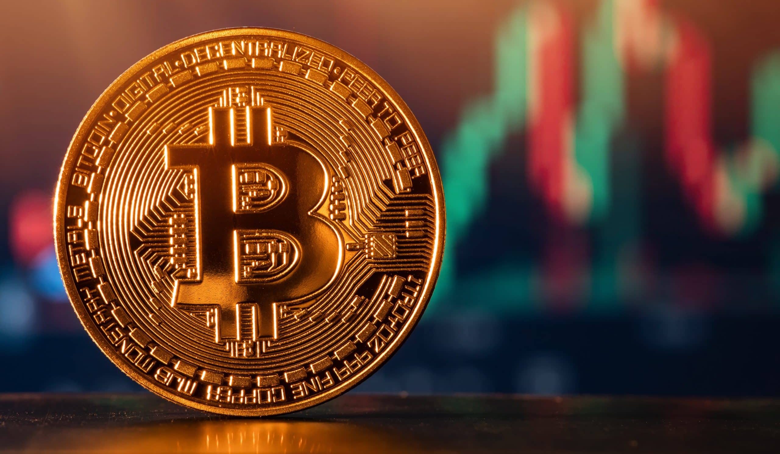 Eine goldene Bitcoin-Münze wird vor einem unscharfen Hintergrund mit bunten Finanzcharts angezeigt.