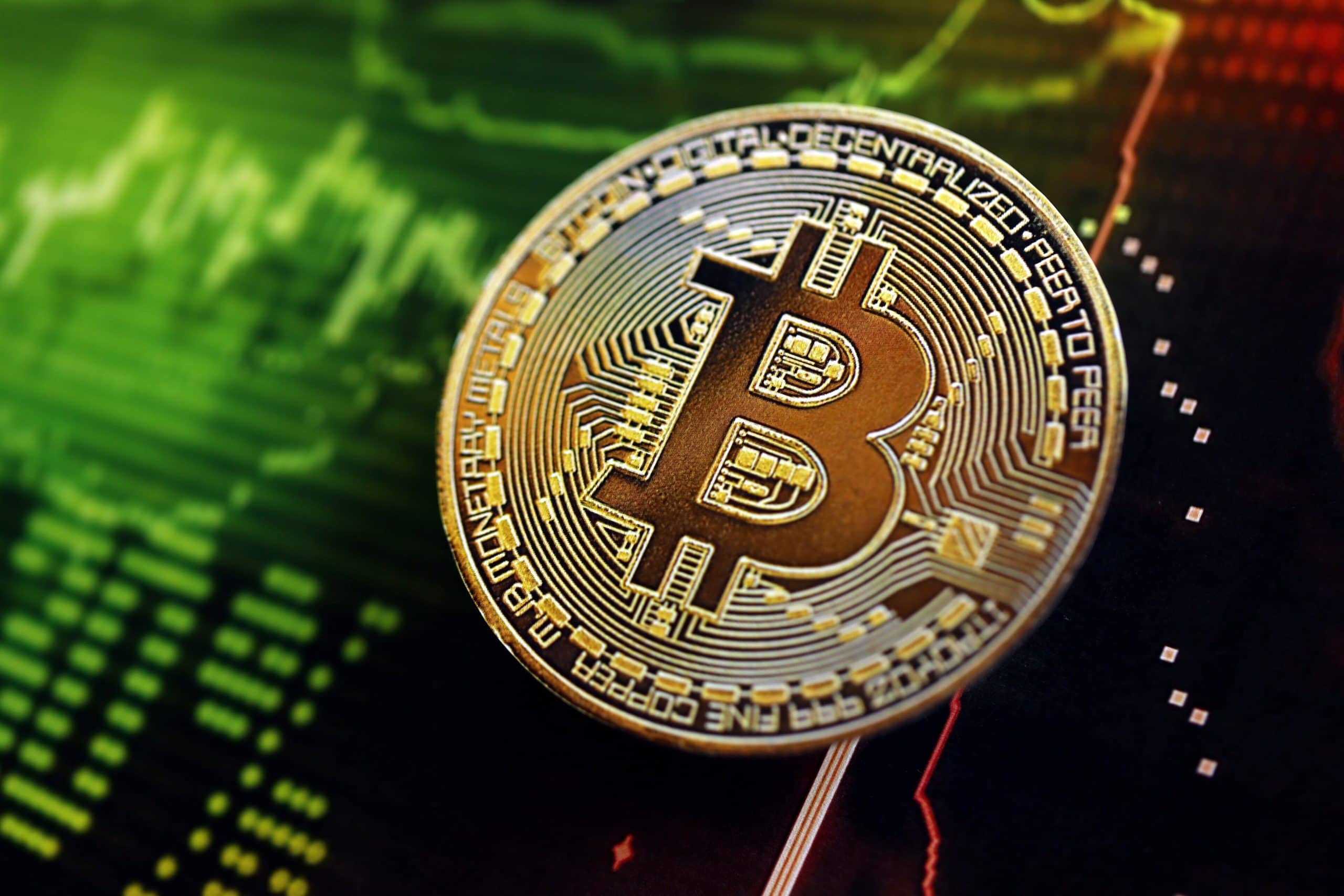 Eine physische Bitcoin-Münze wird über einem digitalen Diagramm gezeigt, das Finanzdaten mit grünen und roten Linien anzeigt.
