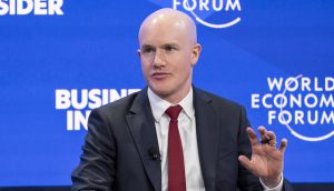 Coinbase-CEO Brian Armstrong in Anzug und roter Krawatte spricht bei einer Podiumsdiskussion mit Logos von Business Insider und dem Weltwirtschaftsforum im Hintergrund über Themen wie den Einfluss von Coinbase und den Aufstieg von BNB in der digitalen Wirtschaft.
