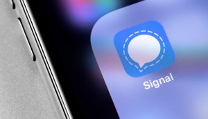 Signal verschlüsselt Nachrichten, sodass sie Dritte nicht auslesen können Nahaufnahme eines Smartphone-Bildschirms mit dem Signal-App-Symbol, das einen blauen Hintergrund mit einer weißen Sprechblase als Symbol für sichere Kommunikation zeigt.