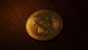 Eine goldfarbene Bitcoin-Münze mit einem großen B-Symbol ruht auf einer dunklen Holzoberfläche unter warmer Beleuchtung und zeigt das ikonische Bitcoin-Design.