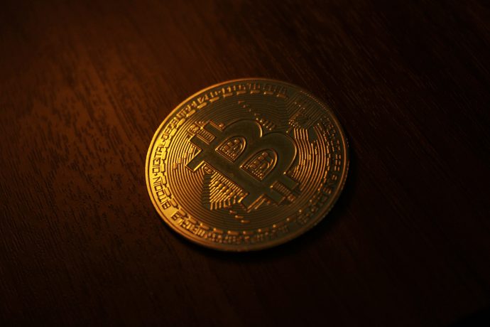 Eine goldfarbene Bitcoin-Münze mit einem großen B-Symbol ruht auf einer dunklen Holzoberfläche unter warmer Beleuchtung und zeigt das ikonische Bitcoin-Design.