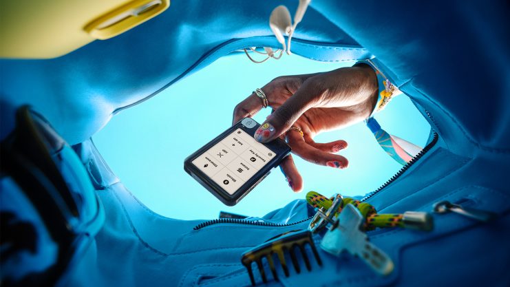 Eine Hand mit lackierten Nägeln hält ein Smartphone, auf dem eine Taschenrechner-App angezeigt wird, und blickt in eine blaue Tasche, die Schlüssel und einen schwarzen Kamm enthält.