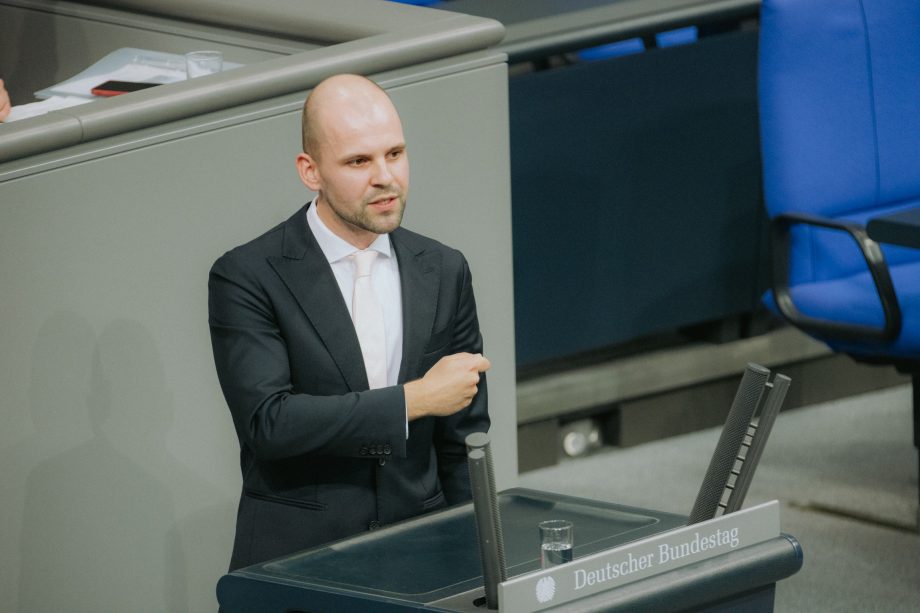 Ein Mann im Anzug steht an einem Podium mit der Aufschrift Deutscher Bundestag und spricht über Bitcoin oder gestikuliert mit seinem rechten Arm in einer formellen Umgebung.