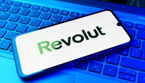 Ein Smartphone mit dem Revolut-Logo liegt auf einer blau beleuchteten Laptop-Tastatur.