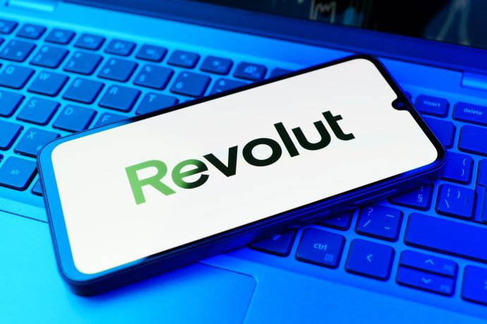 Ein Smartphone mit dem Revolut-Logo liegt auf einer blau beleuchteten Laptop-Tastatur.