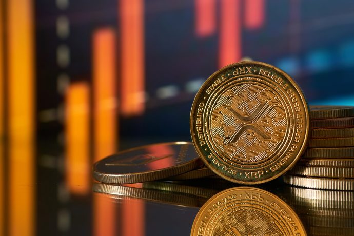 Nahaufnahme von gestapelten XRP-Kryptowährungsmünzen mit orangefarbenem Balkendiagramm im unscharfen Hintergrund, was auf Finanzdaten oder Markttrends hindeutet.